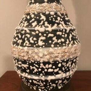 May include: A black and white ceramic table lamp with a textured, speckled glaze. The lamp base has a round, bulbous shape with a brass-coloured metal base.