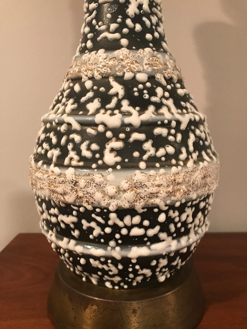 May include: A black and white ceramic table lamp with a textured, speckled glaze. The lamp base has a round, bulbous shape with a brass-coloured metal base.