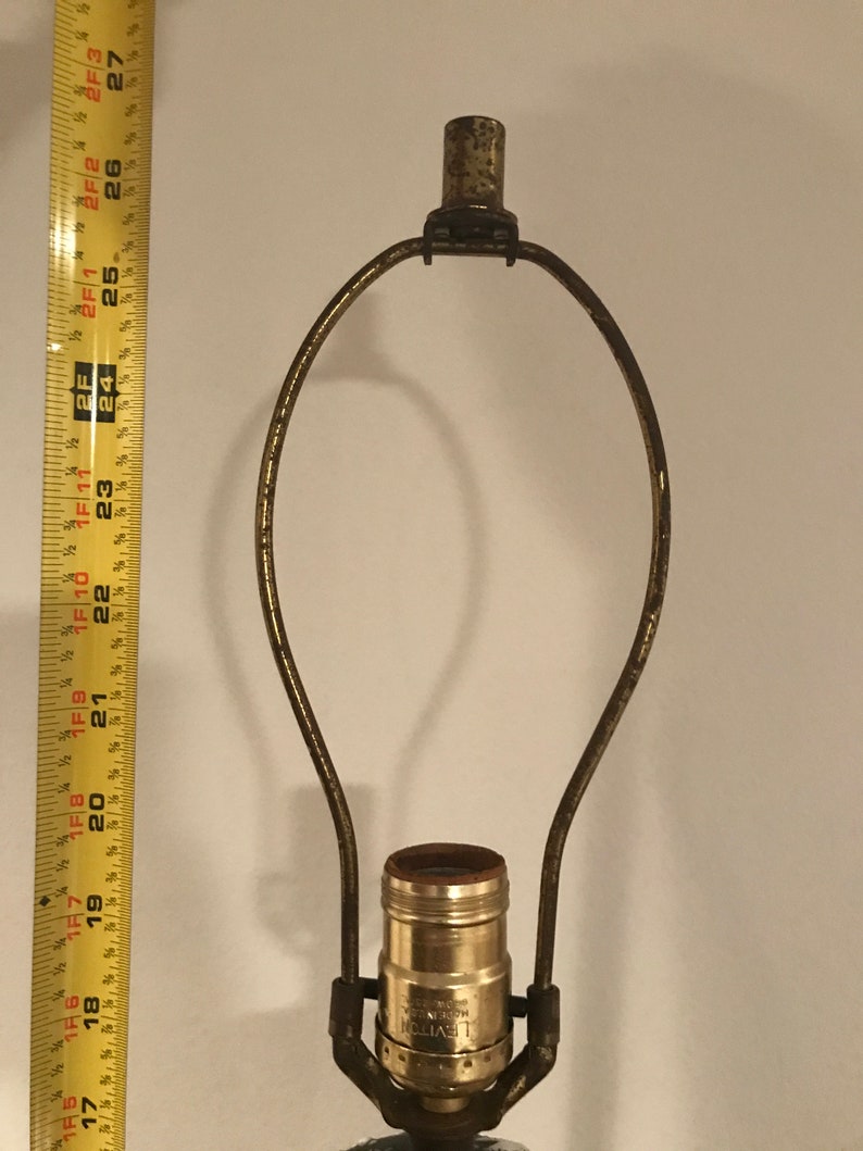 May include: A gold-toned lamp harp with a standard light bulb socket. The socket is labelled "LEVITON MODERN"