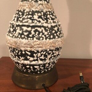 May include: A black and white ceramic table lamp with a textured, speckled glaze. The lamp has a round base and a cord with a plug.