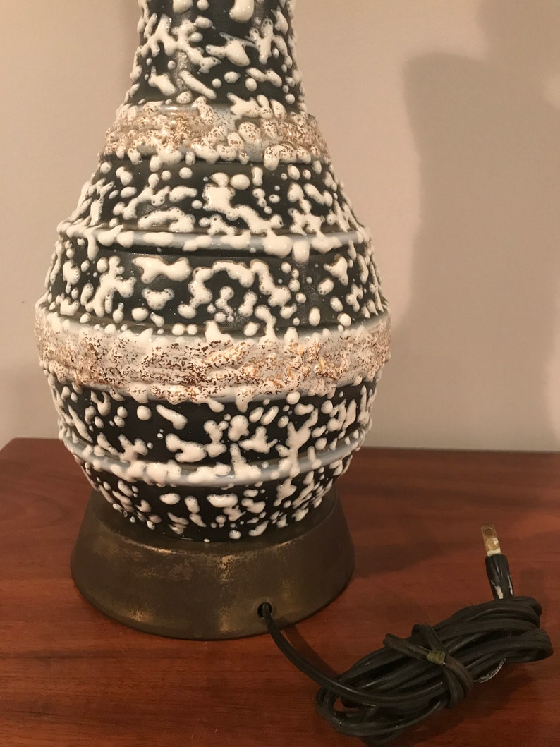 May include: A black and white ceramic table lamp with a textured, speckled glaze. The lamp has a round base and a cord with a plug.