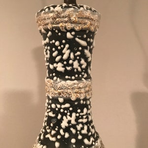 May include: A black ceramic table lamp with white and gold accents. The lamp has a textured surface with a speckled pattern.