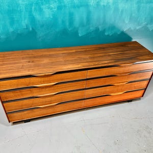 May include: A six-drawer dresser made of dark wood with black accents. The drawers have a curved design and are made of a lighter wood.