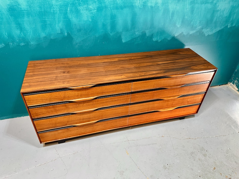 May include: A six-drawer dresser made of dark wood with black accents. The drawers have a curved design and are made of a lighter wood.