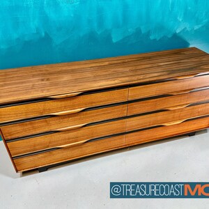 May include: A six-drawer dresser made of wood with a dark brown finish. The drawers have black trim and wooden handles. The dresser is sitting on a light gray floor.