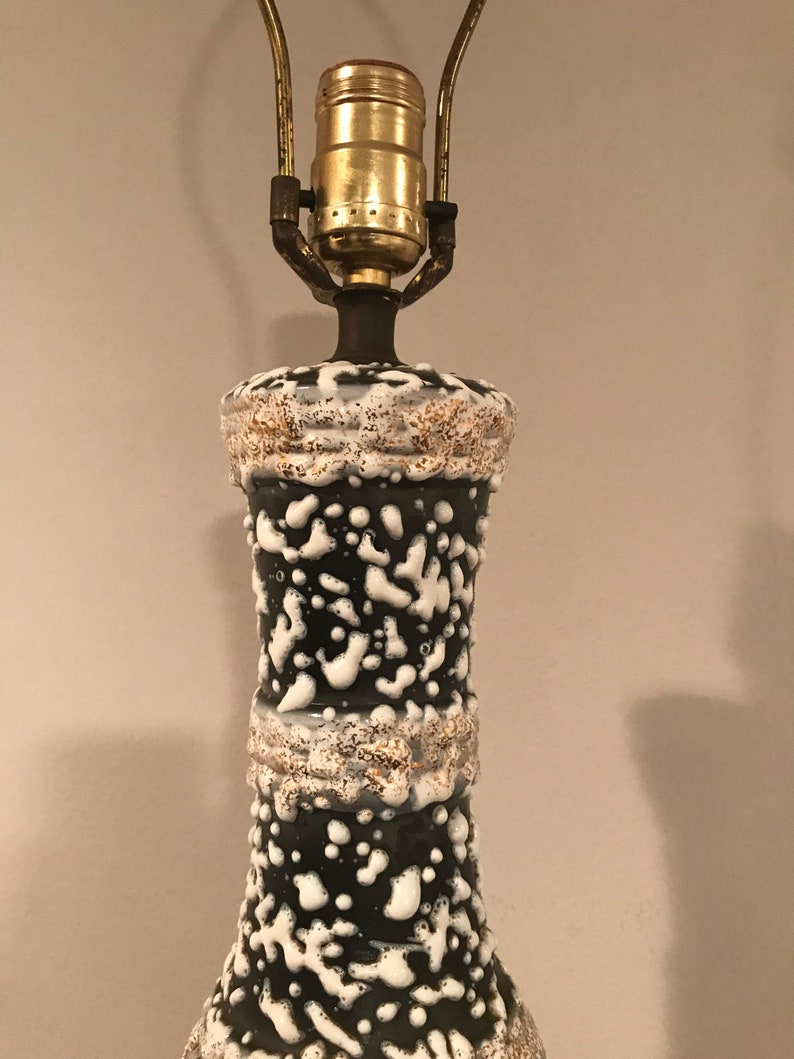 May include: A black and white ceramic table lamp with a textured glaze. The lamp has a gold-coloured socket and a white cord.
