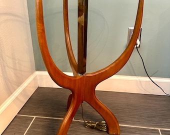 May include: A mid-century modern floor lamp with a glass top table and a brass pole. The base is made of wood and has a unique, organic shape.