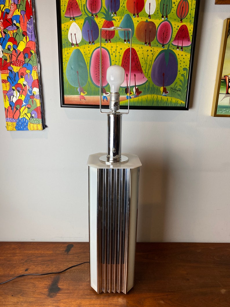 Op de afbeelding: Een chromen tafellamp met een witte, matglazen kap en een geribbelde voet. De lamp heeft een witte gloeilamp en een zwart snoer.