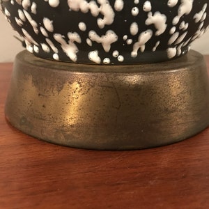 May include: Close-up of the base of a black and white ceramic lamp with a speckled pattern. The base is made of a gold-toned metal.
