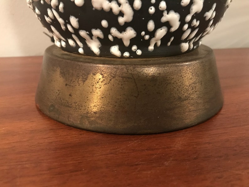 May include: Close-up of the base of a black and white ceramic lamp with a speckled pattern. The base is made of a gold-toned metal.