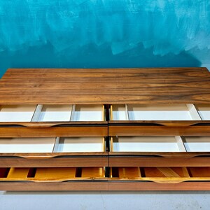 May include: A wooden dresser with six drawers. The drawers are open and the interior is white. The dresser is made of dark wood with a natural wood grain.