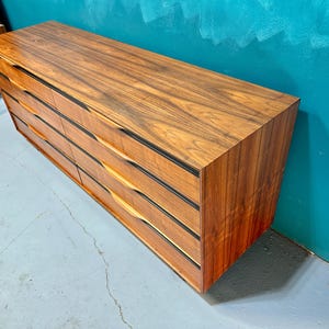 May include: A vintage wooden dresser with six drawers and black trim. The dresser has a rich wood grain pattern and is made of solid wood.