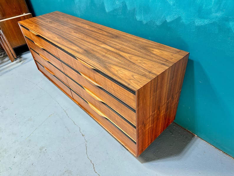 May include: A vintage wooden dresser with six drawers and black trim. The dresser has a rich wood grain pattern and is made of solid wood.