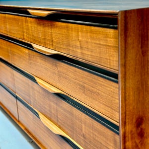 May include: A vintage wooden dresser with six drawers and black trim. The drawers have unique curved wooden handles.