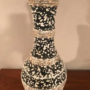 May include: A black and white ceramic table lamp with a textured, speckled glaze. The lamp has a wide base and a narrow neck.