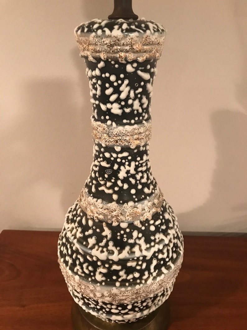 May include: A black and white ceramic table lamp with a textured, speckled glaze. The lamp has a wide base and a narrow neck.
