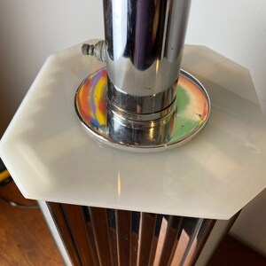 Op de afbeelding: Een chromen en witte tafellamp met een gegroefde basis en een ronde, achthoekige bovenkant. De lamp heeft een chromen fitting en een wit snoer.