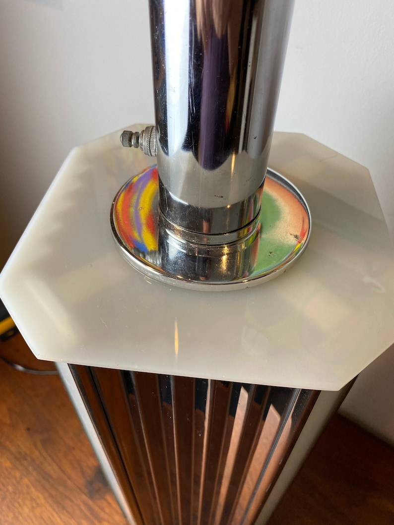 Op de afbeelding: Een chromen en witte tafellamp met een gegroefde basis en een ronde, achthoekige bovenkant. De lamp heeft een chromen fitting en een wit snoer.