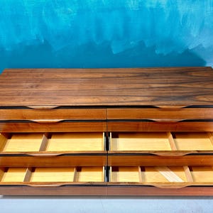 May include: A six-drawer dresser made of dark wood with a wood grain pattern. The drawers are open and show the light wood interior.