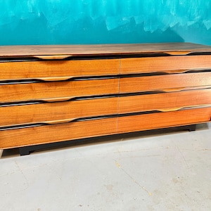 May include: A six-drawer dresser made of wood with a dark brown finish. The drawers have black trim and wooden handles.