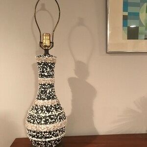 May include: A black and white ceramic table lamp with a brass base and a white cord. The lamp has a white and black speckled design with a band of white around the middle.