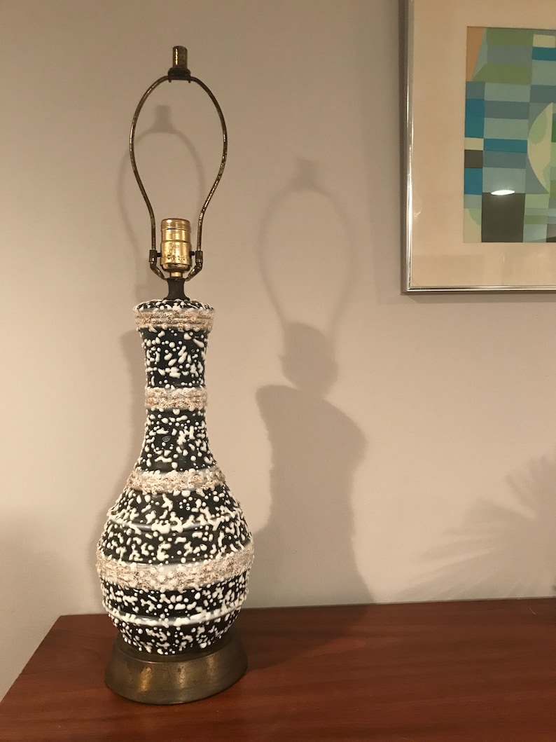 May include: A black and white ceramic table lamp with a brass base and a white cord. The lamp has a white and black speckled design with a band of white around the middle.