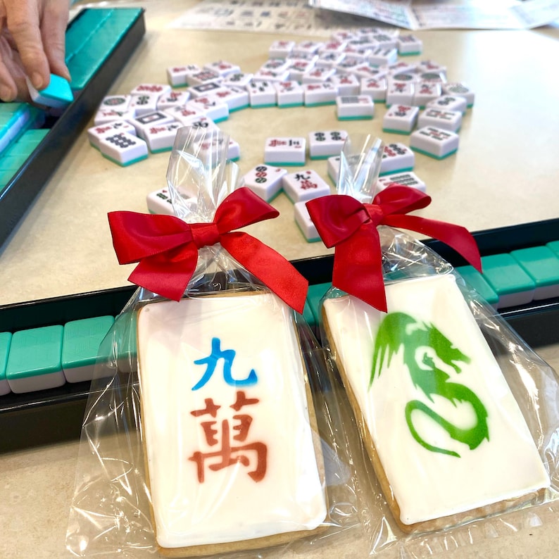 May include: Two decorated cookies in clear plastic bags tied with red ribbons. One cookie has a green dragon design and the other has Chinese characters that read "Nine Bamboo".