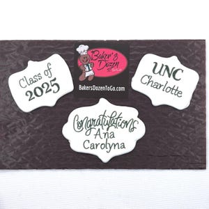 May include: Three white, scalloped-edge cookies with dark text. One reads Class of 2025, another UNC Charlotte, and the third Congratulations Ana Carolyna. A square black logo with a gingerbread person and Baker's Dozen To Go is centered.