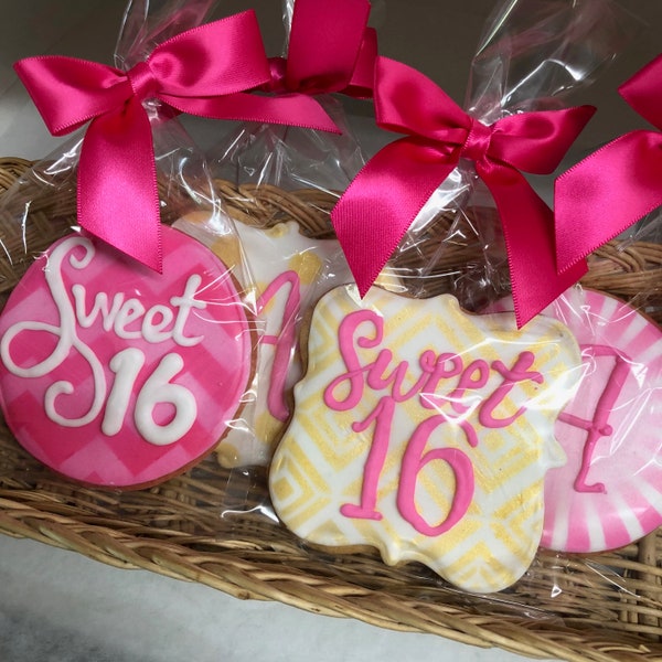 Könnte beinhalten: Kekse mit rosa und weißem Zuckerguss, verpackt in transparenten Zellophanbeuteln und mit leuchtend rosa Satinbändern gebunden. Die Kekse haben die Form von Kreisen und einer einzigartigen Form, mit den Worten "Sweet 16" darauf geschrieben.