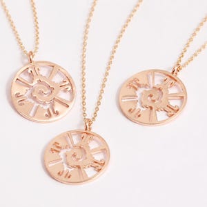 May include: Three rose gold necklaces, each featuring a circular pendant with a central spiral design surrounded by radiating cut-out segments. The pendants are suspended from delicate matching rose gold chains with a polished metallic finish.