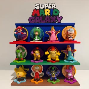 May include: A blue, multi-tiered display shelf with Super Mario Galaxy figurines. The shelf has red and green shelves and a brown base. The top displays the words "SUPER MARIO GALAXY". The figurines include Mario, Yoshi, and Princess Peach.