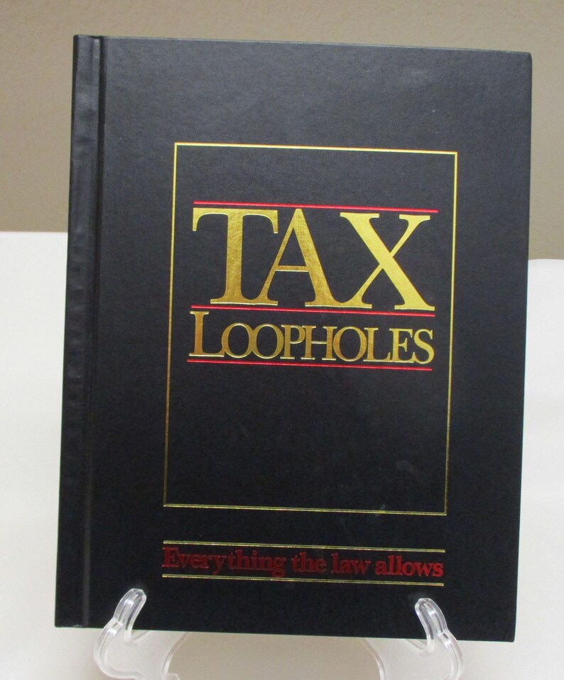 May include: A black book titled "TAX LOOPHOLES" with gold lettering and a red underline. The text "Everything the law allows" is printed in red at the bottom. The book is displayed on a clear stand.