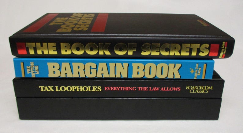 May include: A stack of three books with titles in gold lettering. The top book is black with "THE BOOK OF SECRETS" on the cover. The middle book is blue with "BARGAIN BOOK". The bottom book is black with "TAX LOOPHOLES".