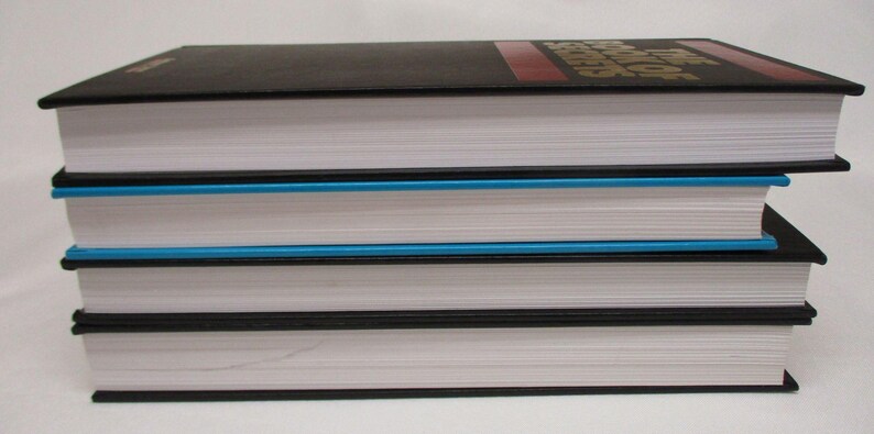 May include: A stack of three hardcover books with white pages and black covers. The top book has a red stripe and gold lettering. The middle book has a blue edge. The books are stacked on top of each other.