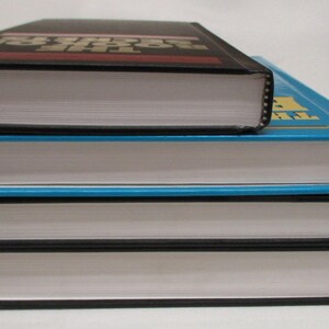 May include: A stack of three hardcover books with white pages and black or blue covers. The top book is black with red text, the middle book is blue, and the bottom book is black.