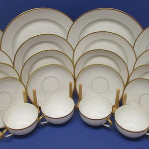 May include: A complete white porcelain dinnerware set with gold trim. The set includes plates, saucers, and teacups. The plates are arranged in a fan shape, showcasing the elegant design. This set is perfect for formal dining.
