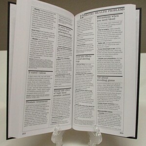 May include: An open book with black covers, held upright by a clear stand. The pages are filled with small text, with the chapter title "12 SOLVING HEALTH PROBLEMS" visible. The book is likely a health or medical guide.