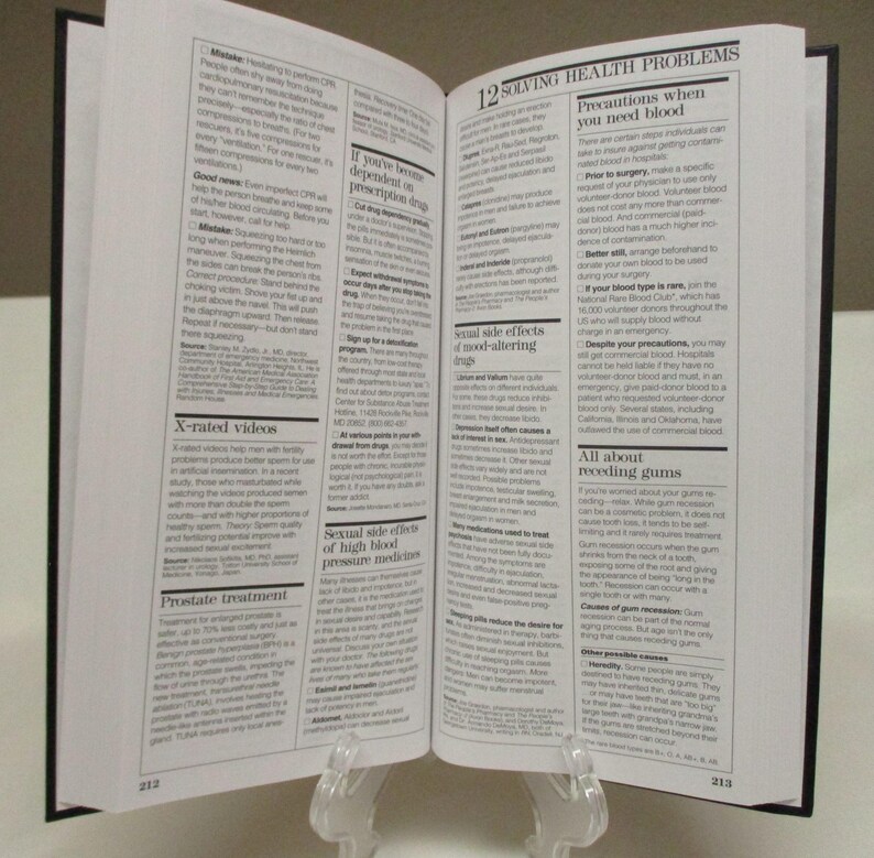 May include: An open book with black covers, held upright by a clear stand. The pages are filled with small text, with the chapter title "12 SOLVING HEALTH PROBLEMS" visible. The book is likely a health or medical guide.