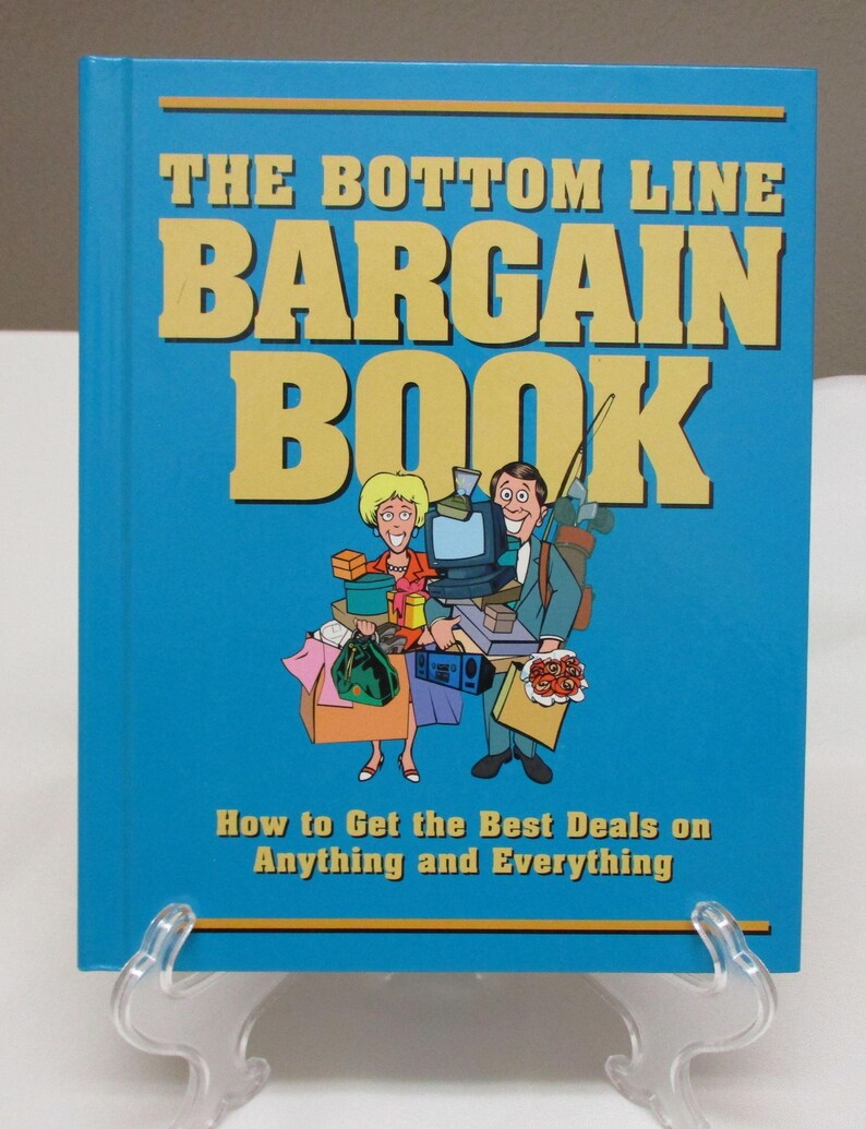 May include: A hardcover book titled "THE BOTTOM LINE BARGAIN BOOK" with a blue cover and yellow lettering. The cover features an illustration of a man and woman carrying shopping bags and other items. The subtitle reads "How to Get the Best Deals on Anything and Everything."