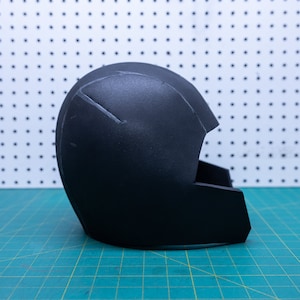 May include: A black foam helmet with a visor, partially assembled. The helmet is sitting on a green cutting mat.
