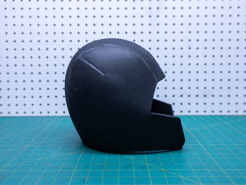 May include: A black foam helmet with a visor, partially assembled. The helmet is sitting on a green cutting mat.