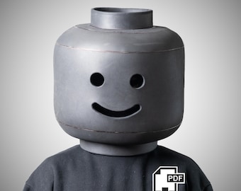 May include: A matte dark grey head-shaped mask featuring a cylindrical top protrusion, two circular eye cutouts, and a curved mouth cutout. The mask is worn over a plain black long-sleeved shirt. A white icon with the text PDF is visible.
