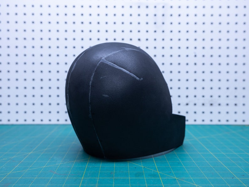May include: A black foam helmet with white lines drawn on it. The helmet is sitting on a green cutting mat.