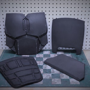 Puede incluir: Cuatro piezas de armadura gris oscuro, posiblemente para cosplay o un disfraz. Las piezas incluyen una placa para el pecho, una placa para la espalda y dos componentes m&aacute;s peque&ntilde;os. La armadura est&aacute; hecha de un material r&iacute;gido y tiene costuras visibles.