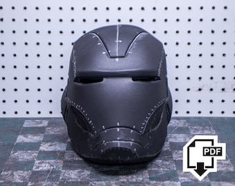 Pode incluir: Um capacete preto com um design detalhado e uma superfície texturizada. O capacete tem uma viseira e uma queixeira. O capacete está sentado em uma superfície quadriculada.