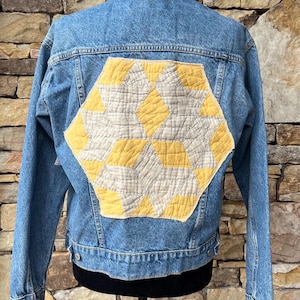 May include: A blue denim jacket with a yellow and white quilted patch on the back.