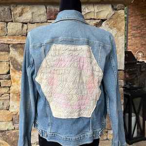 May include: A blue denim jacket with a hexagonal patchwork design on the back. The patchwork is made of beige and pink fabric with a geometric pattern.