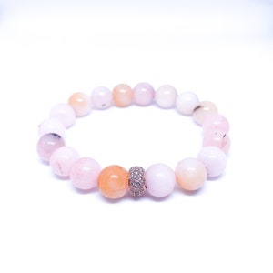 May include: A pink and orange gemstone bracelet with a rose gold and clear crystal accent bead.