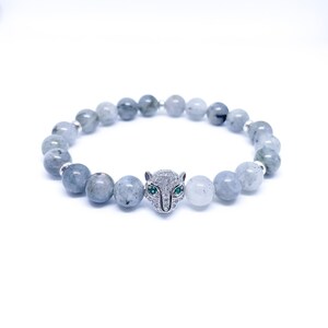 May include: A gray gemstone bracelet with a silver panther charm featuring green eyes and white accents.