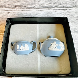 Può includere: Un set di brocca per la panna e zuccheriera in porcellana blu e bianca con un motivo floreale bianco. Il set è in una scatola nera con imbottitura in schiuma bianca.